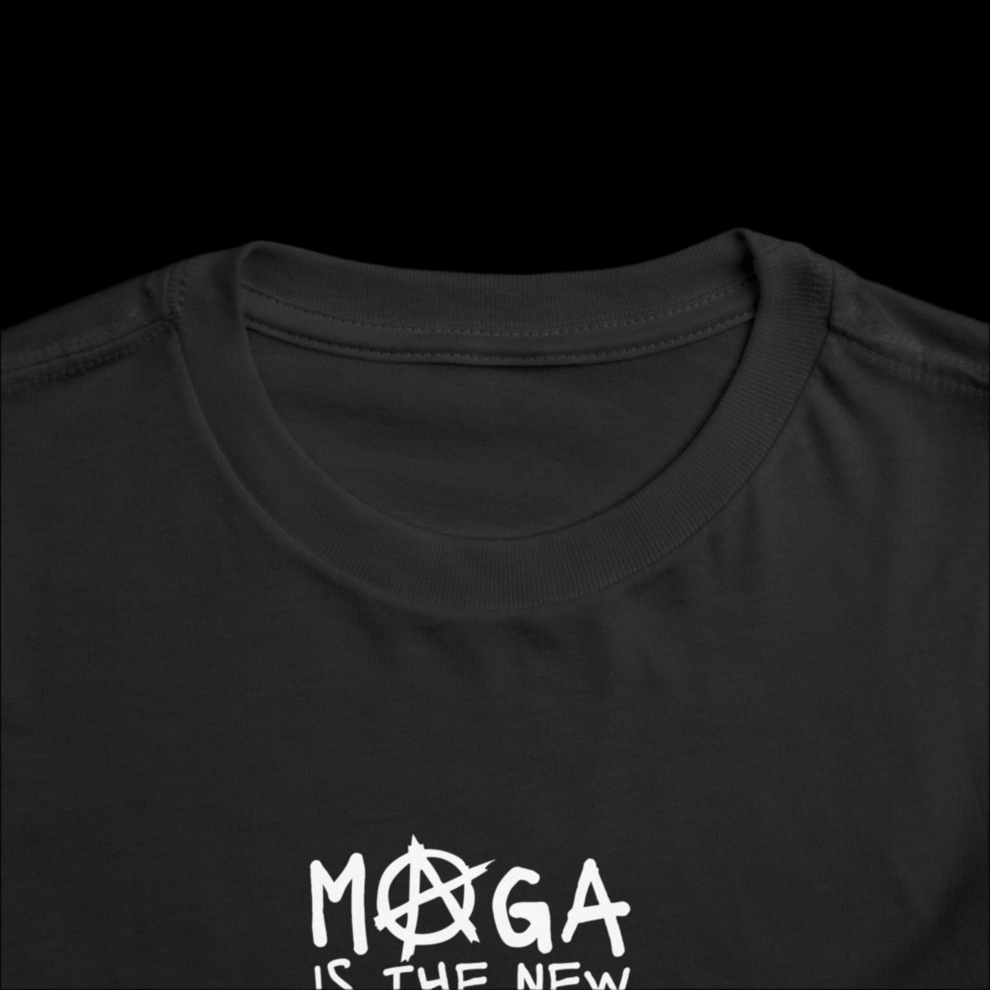 Close-up of a black graphic tee with the phrase MOGA IS THE NEW in white text on the front. The letter A in MOGA is uniquely stylized with an anarchy symbol. This short sleeve design captures a bold statement, perfect for trendsetters of all ages.