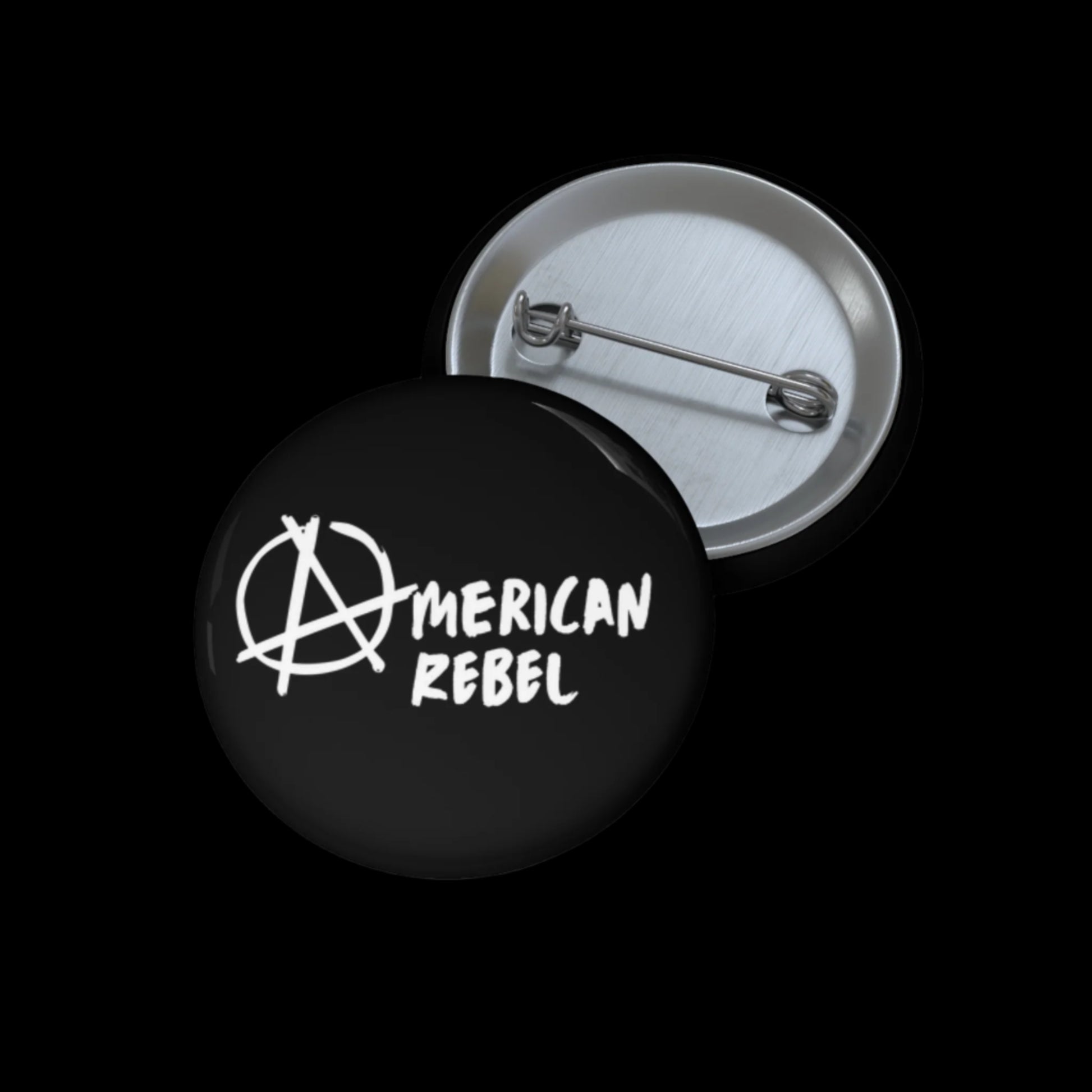 A black circular pin-back button, UV resistant and proudly assembled in the USA, features the words American Rebel written in white with an anarchy symbol replacing the A. The button is displayed with its clasp visible.