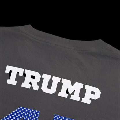 A graphite, garment-dyed t-shirt features TRUMP boldly in large white letters across the back. Blue numbers below adorned with white stars suggest a sports jersey influence.