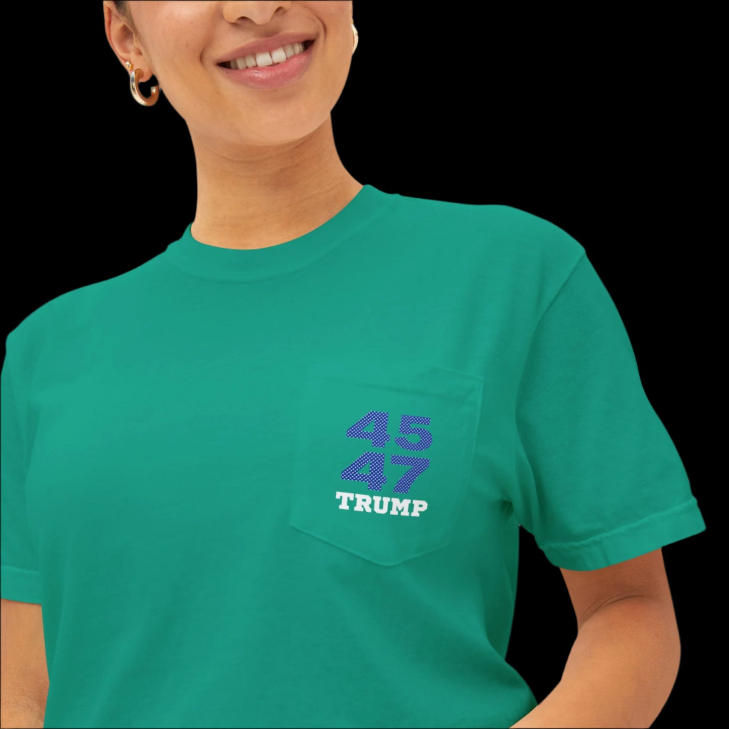 A smiling woman wearing a garment-dyed island green T-shirt featuring the numbers 45 and 47 alongside the word Trump on the pocket, reminiscent of sports jersey t-shirts.