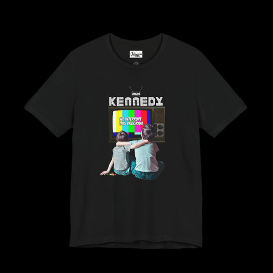 A black graphic short sleeve tee showcases two kids in front of a vintage TV displaying a color test pattern, with "We interrupt this program" and KENNEDY 2024 boldly printed above—perfect for fans of RFK Jr.'s MAHA movement