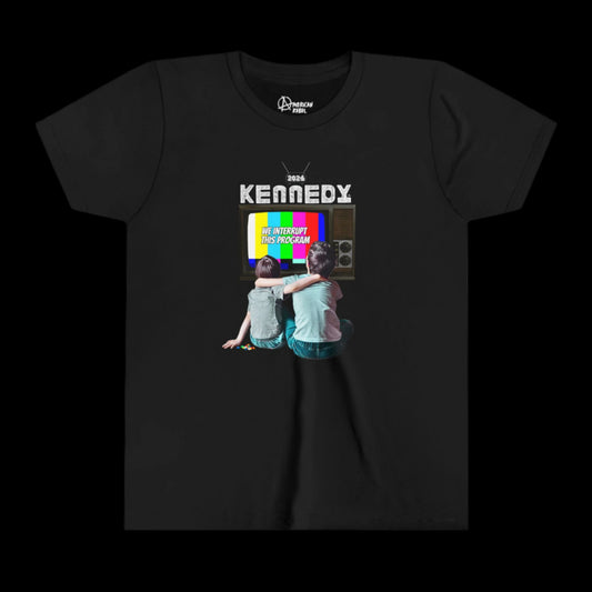 This Youth Graphic Tee is 100% cotton and sports a black design showcasing two children seated in front of a vintage television with colorful bars, above which KENNEDY is boldly displayed. The text WE INTERRUPT THIS PROGRAM enhances its unique appeal.