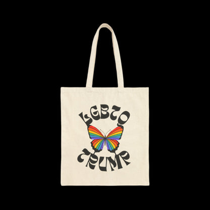 A natural white cotton canvas tote bag showcases a vibrant rainbow-colored butterfly at its center. Encircling the butterfly are the words LGBTQ- TRUMP in bold, artistic font, all set against a solid black background.