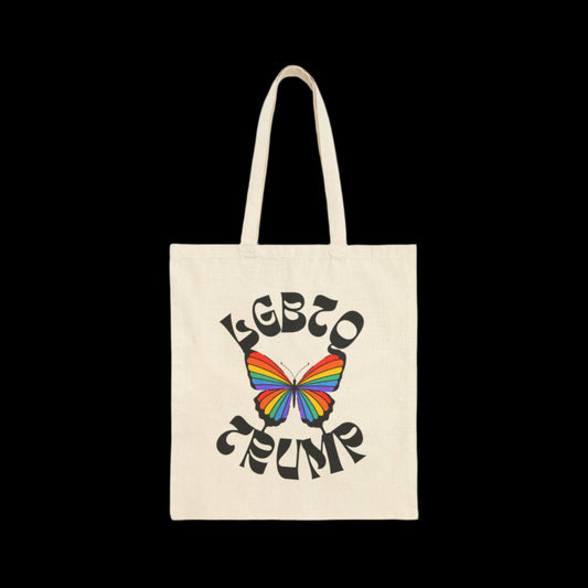 A natural white cotton canvas tote bag showcases a vibrant rainbow-colored butterfly at its center. Encircling the butterfly are the words LGBTQ- TRUMP in bold, artistic font, all set against a solid black background.