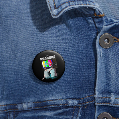 A black button on a denim jacket showcases two people sitting with their backs to a vibrant TV screen, above which KENNEDY is displayed. This RFK Jr.-Kennedy TV-Pin is not only scratch and UV resistant but also proudly assembled in the USA.