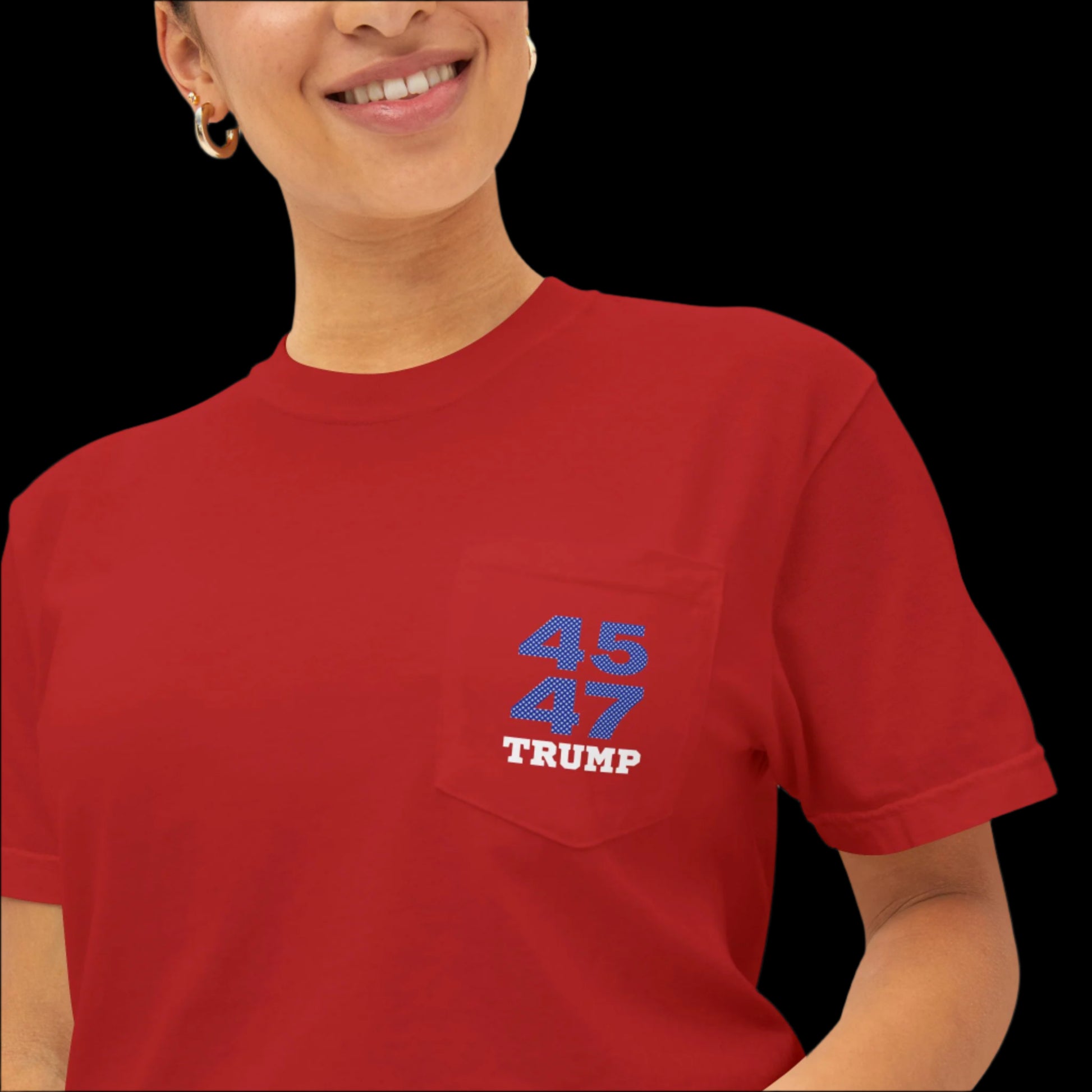 A smiling person wearing a garment-dyed red T-shirt with Trump 45 47 in bold blue and white text on the pocket, giving it the look of a sports jersey t-shirt.