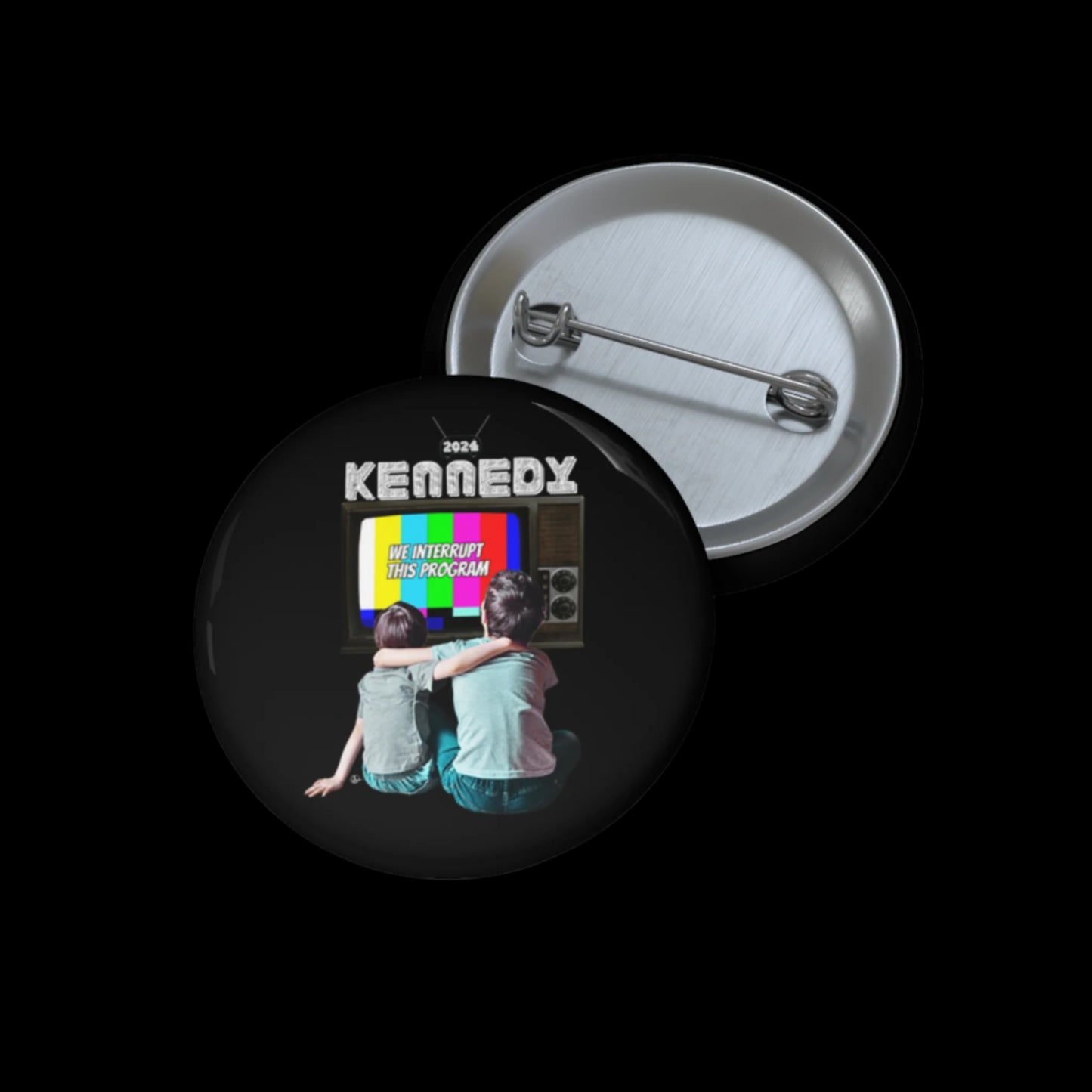 A circular pin badge featuring two children from behind watching a vintage TV with a We Interrupt This Program screen. Text above reads Kennedy 2024. The badge, assembled in the USA, is scratch and UV resistant and has a metal pin on the back.