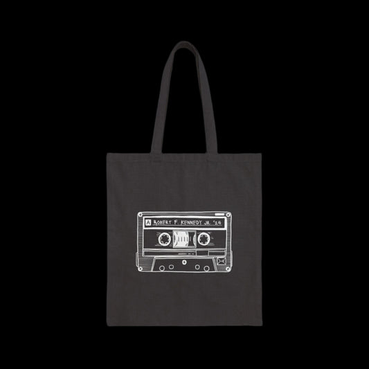 A black tote bag crafted from 100% cotton canvas showcases a white line drawing of a cassette tape. The label reads Robert Kennedy Jr '24. The solid black background highlights its vintage charm.