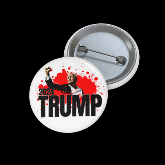 A pin button showcasing the 2024 TRUMP graphic of Donald Trump with a fist pump, set against a red splatter background. Assembled in the USA, this eye-catching button rests open on a sleek black surface.