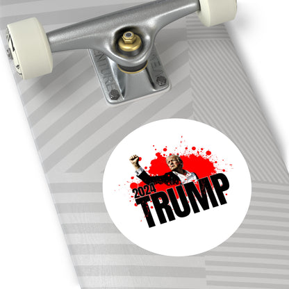 A skateboard deck boasting a diagonal stripe pattern and a premium vinyl sticker. The sticker displays the word TRUMP in bold, accompanied by a photo of Trump raising his fist above 2024, all surrounded by red splatter for an edgy look.