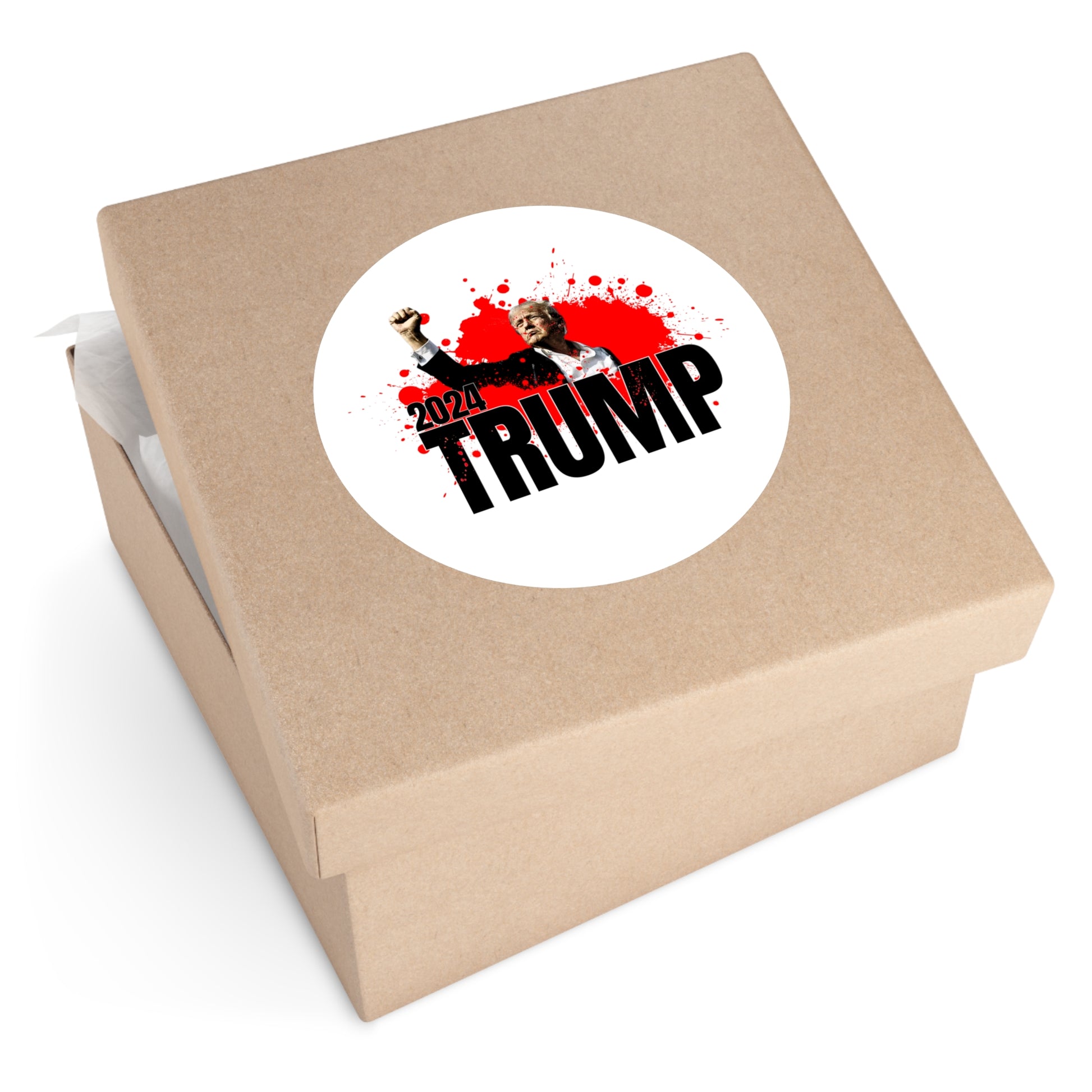 A brown gift box features a premium vinyl round sticker on the lid with a 2024 election design. The sticker shows Trump in a suit, raising his fist, with TRUMP bolded and red blood splatter effects in the background.