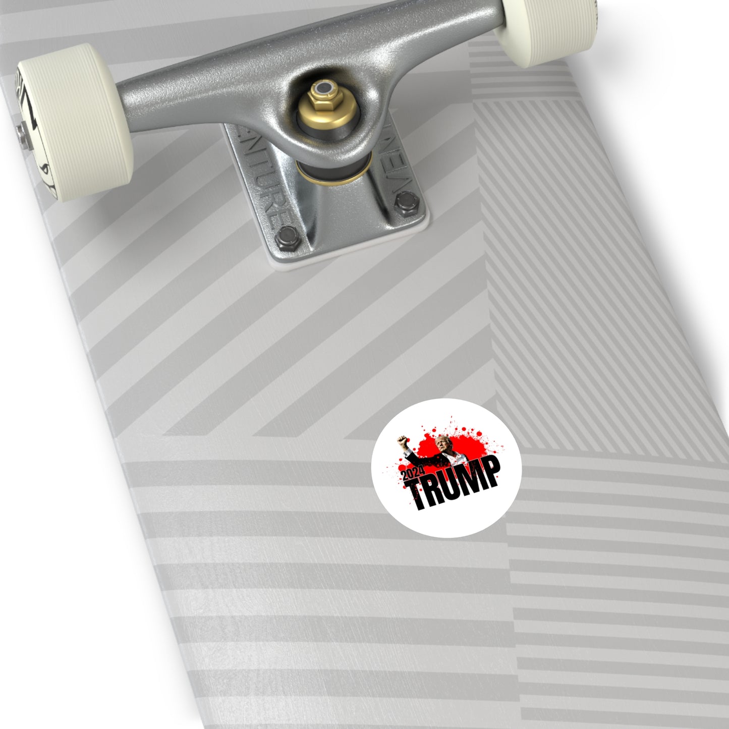 Close-up of a skateboard deck showcasing the truck and wheels. The deck flaunts a geometric pattern in shades of gray, with a premium vinyl sticker depicting Donald Trump raising his fist and the text TRUMP 2024 on a red splatter background.