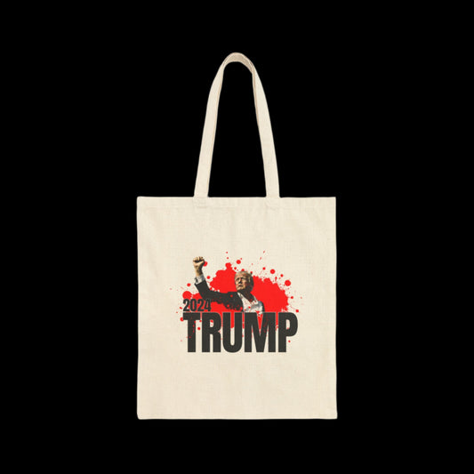 This 100% cotton canvas tote bag showcases a striking graphic of Donald Trump in a suit with an arm raised in a fist. Adorned with red blood splatter and the year 2024, it prominently features the text TRUMP against a black background, making it both durable and bold.