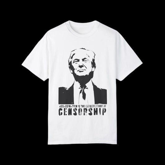 This vintage tee is crafted from ethically grown cotton, showcasing a black-and-white graffiti style stencil image of Donald Trump in a suit with a grin on his face. Beneath the image, the text reads: ASSASSINATION IS THE EXTREME FORM OF CENSORSHIP. The relaxed fit adds comfort and style.