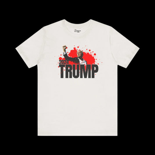 This Unisex Jersey Short Sleeve T-shirt showcases a bold graphic of Trump in a suit with a raised fist, set against red splatters. Emblazoned with 2024 TRUMP, it captures the essence of the iconic political assassination attempt of Donald Trump.