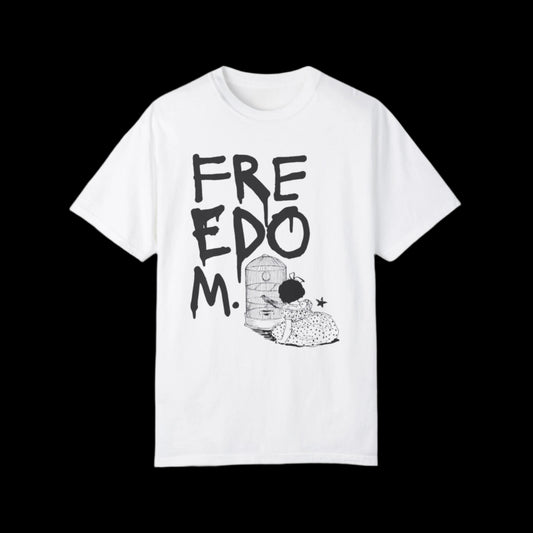 A white t-shirt featuring FREEDOM in bold black graffiti spray paint letters, with a punk art-style cartoon of a child unlocking a birdcage.