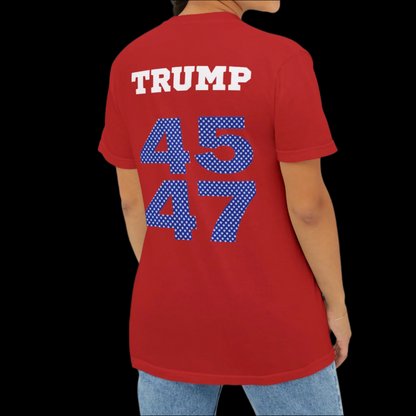 A woman is sporting a garment-dyed, red T-shirt featuring TRUMP alongside the large polka-dotted numbers 45 and 47 on the back, reminiscent of sports jersey T-shirts, paired with blue jeans.