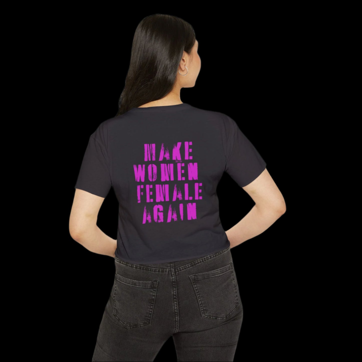 A woman with long dark hair stands with their back to the camera, wearing a black crop top adorned with pink capital letters that read MAKE WOMEN FEMALE AGAIN. Theyre paired with dark jeans, creating a bold statement in support of feminism and womens rights.