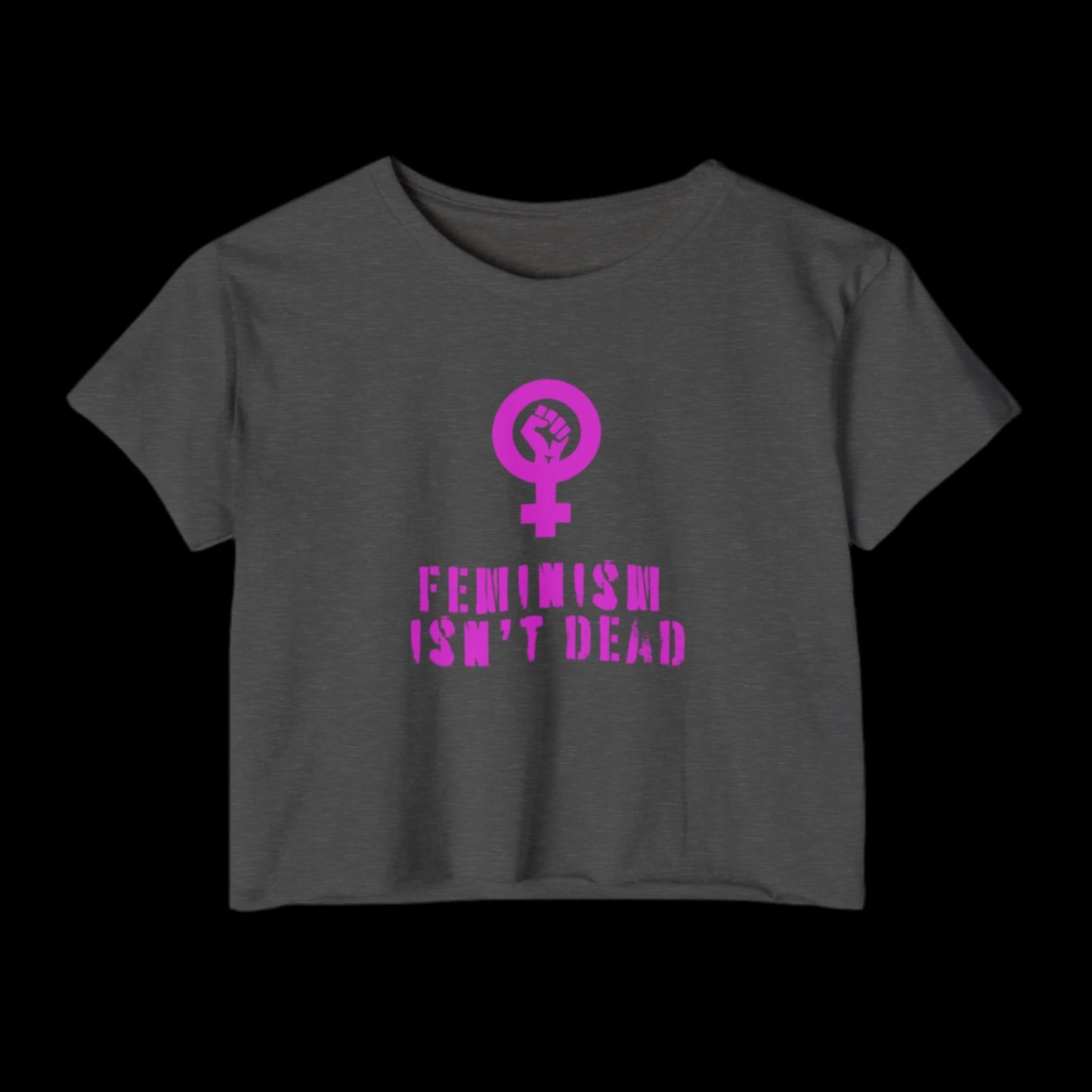 A charcoal gray crop top with a pink female gender symbol incorporating a raised fist celebrates Women's Rights. Below the symbol, in bold pink text, it reads Feminism Isn't Dead. The shirt stands out against a black background.