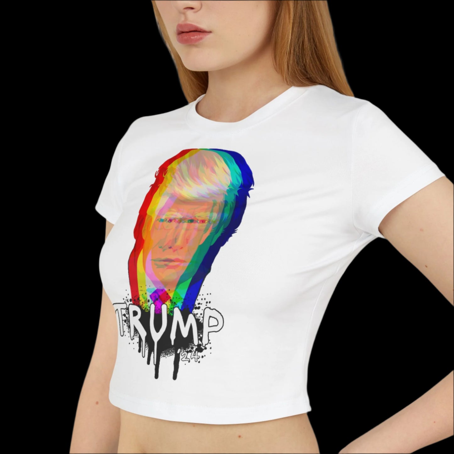 A person wearing a white baby tee made from organic cotton, featuring graffiti art with a colorful, abstract illustration of Donald Trump's face. The bold design reads TRUMP with a paint splash effect below. The background is completely black.